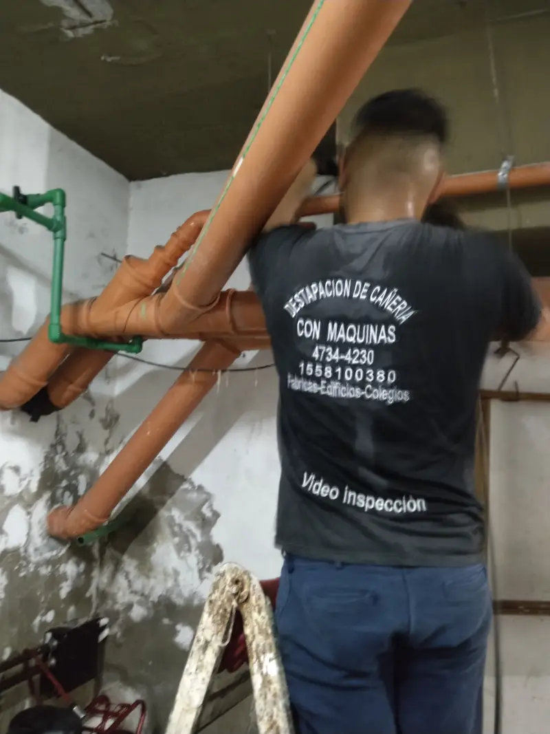 Técnico de Destapaciones OB realizando conexión de cañería cloacal aérea en subsuelo de edificio