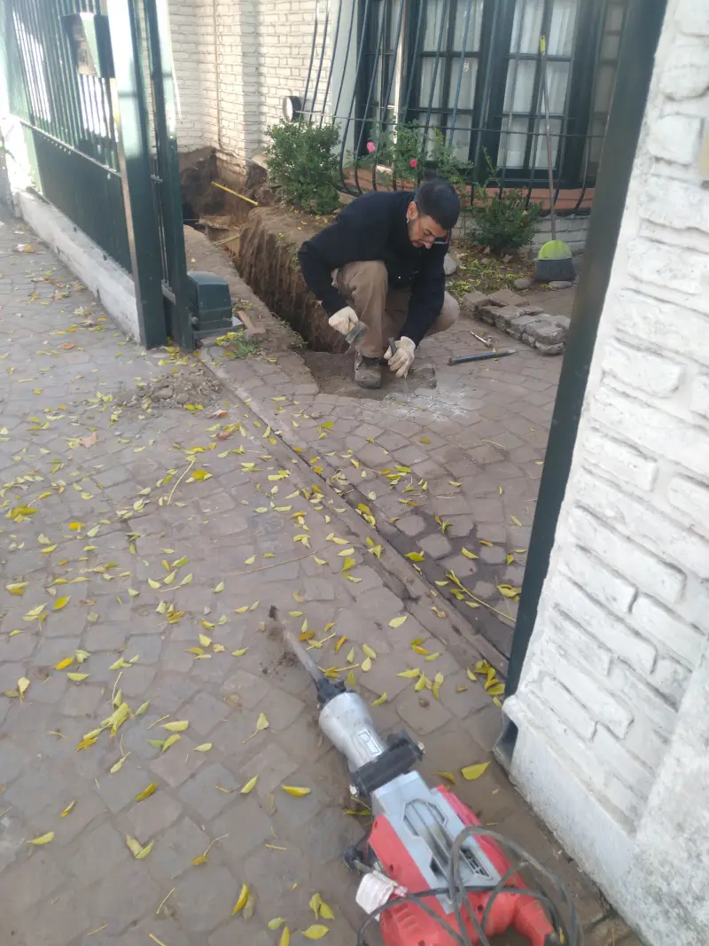 Especialista reparando cañería pluvial enterrada en entrada de vivienda en GBA